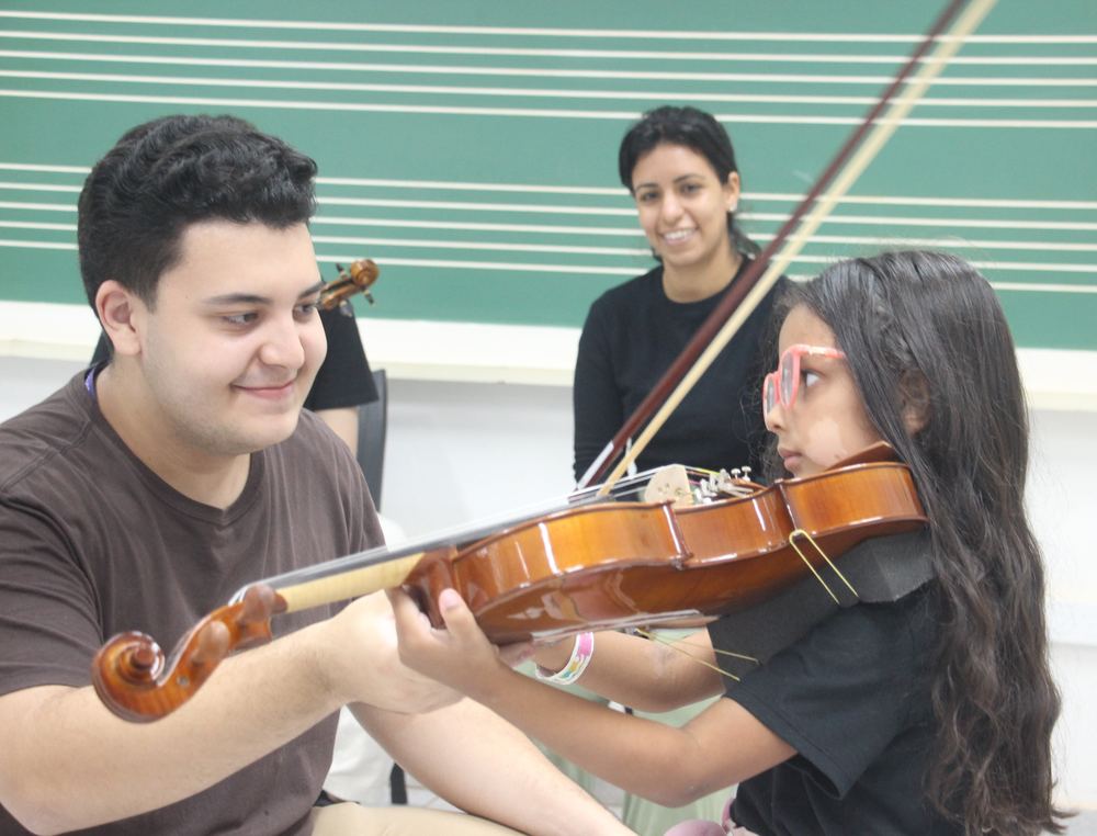 Jovem ensinando violino a uma criança em sala de aula